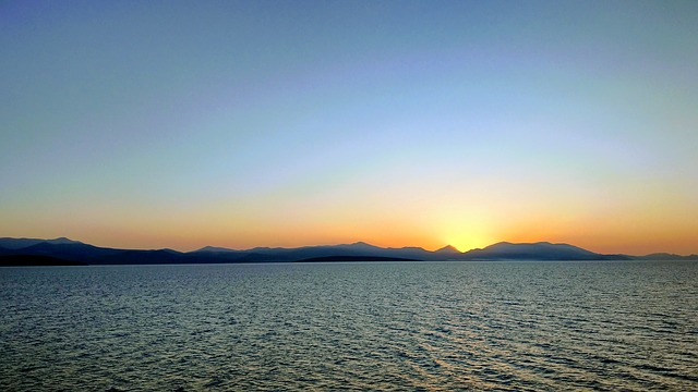 A sunset over the ocean with mountains in the background.