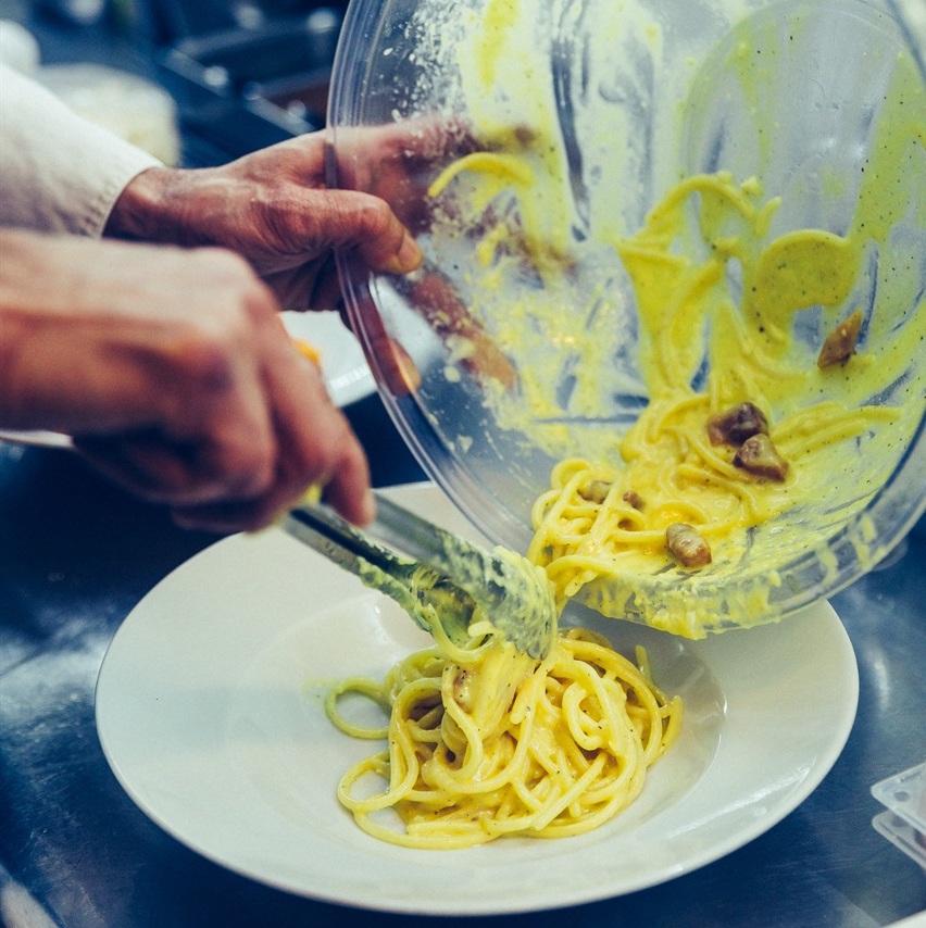 A person using a knife and fork to cut pasta.