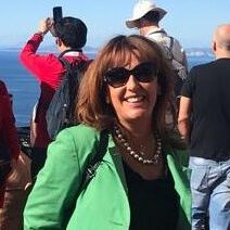 A woman in green jacket standing next to the ocean.